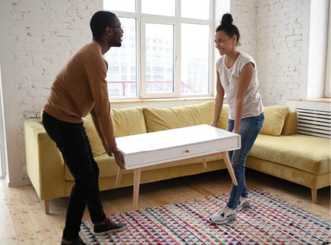 Young happy african american couple moving wooden table. Attractive family of diverse woman and man relocation furniture in new flat. Husband and wife perform permutation. First time buyers